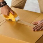 Unrecognizable man sealing box with duck tape while preparing for moving out