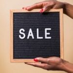 Close-up of hands holding a 'SALE' sign against a beige background, perfect for promotional use.